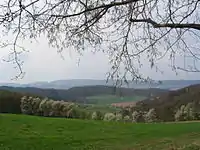 Blick von Böllstein (Wallbrunn) über Gneis-Hügel (rechts: Schnellerts, links: Eichberg-Rücken) und das Gesprenztal zum Flasergranitoid-Höhenzug Neunkircher-Höhe-Nonrod, links davon: Lindenfelser Granit-Diorit-Gabbro-Berge (Schenkenberg, Das Buch)