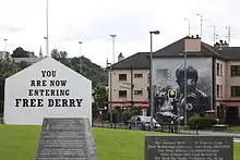 Wandbild des jungen Jimmy Porters, ein Widerstandskämpfer während der Unruhen im August 1969 mit Gasmaske und Molotowcocktail zudem erkennt man an seiner Jacke einen Umriss von Nordirland. sowie Wandbild – „Sie betreten das freie Derry“