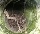 Blick in den Burgbrunnen. Der etwa 10&nbsp;Meter tiefe Schacht ist ungefähr bis zur Hälfte verschüttet. Zusätzlich zum Schichtenwasser wurde ehemals Regenwasser eingeleitet