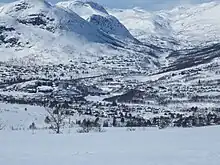 Foto einer verschneiten Berglandschaft, mit einer Ortschaft im Tal