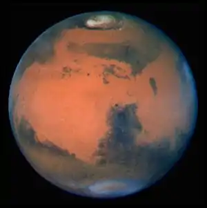 Aufnahme des Mars mit dem Hubble-Weltraumteleskop. Syrtis Major ragt von Süden (unten) in die helleren Regionen hinein