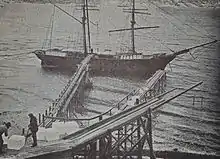 Eisblöcke werden über zwei Rutschen auf ein Segelschiff befördert.