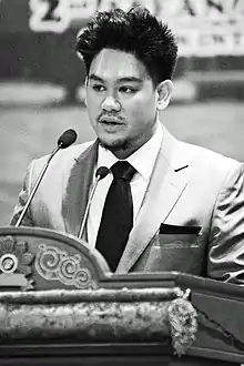 Prinz Azim beim ASEAN Autism Network Congress. Schwarz-Weiß-Bild eines malaiischen jungen Mannes mit hochgegelten Haaren im hellen Anzug, 2013.