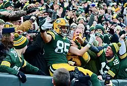 Robert Tonyan, Spieler der Green Bay Packers, sitzt zwischen jubelnden Fans auf der Tribüne, nachdem er auf diese gesprungen ist