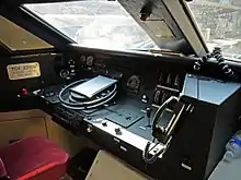 Schräg seitliches Foto von innen auf den Führerstand eines TGV-Sud-Est-Triebkopfs. Im Vordergrund auf einem schwarzen Tisch die Bedienelemente, im Hintergrund eine zweigeteilte Frontscheibe. Auf einem Schild steht die Triebzugnummer: TGV 23129
