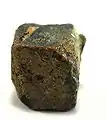 Rutherfordin (gelblichbrauner Belag) auf Uraninit aus dem Ulugurugebirge, Tansania (0,9&nbsp;cm × 0,8&nbsp;cm × 0,7&nbsp;cm)