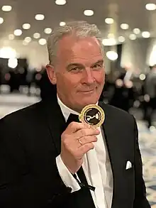 Volker Schmidt-Sondermann bei den International Emmy Awards in New York, 2023 (Nominierung „Triff... Anne Frank“). Volker Schmidt-Sondermann zeigt eine Nominierten-Medaille.