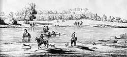A small wooden raft in the middle of a river which runs through a flat rural landscape.
