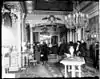 The interior of a home with several people gathered, but wearing winter coats. Ornate decorative features such as chandeliers and fancy rugs are visible