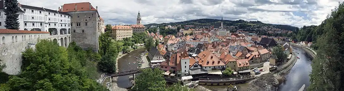 Blick auf die historische Altstadt von Český Krumlov im Juli 2013 vom Schloss aus. Links die Mantelbrücke und der Burgturm, in der Mitte die St.-Veit-Kirche, davor die Moldauinsel. Ungefähr da, wo der Bagger steht vor dem Wehr, zweigt der Kanal unter dem Wasserwerk ab.