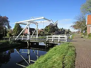 Szene in Großefehn: Eine der charakteristischen, weißen Klappbrücken am Kanal, Klinkerbauten und im Hintergrund eine Windmühle.